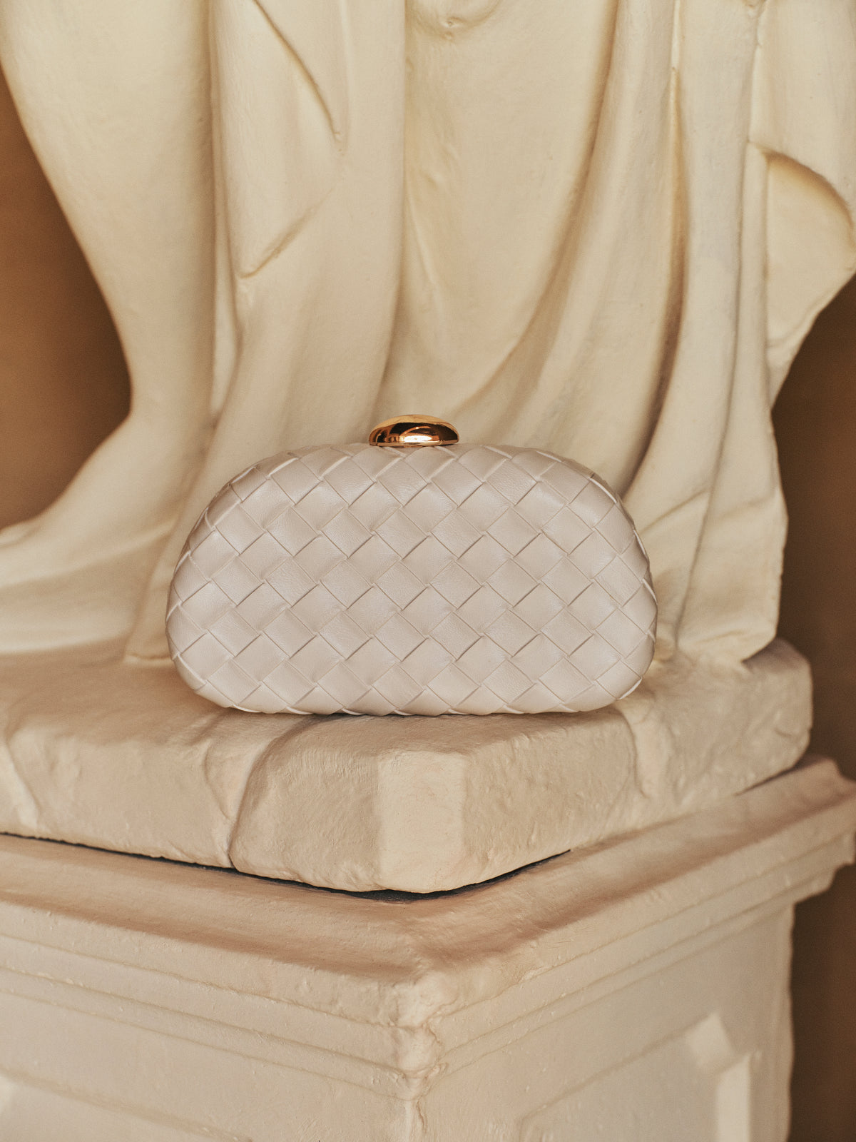 a white purse with a gold ring on top of a statue